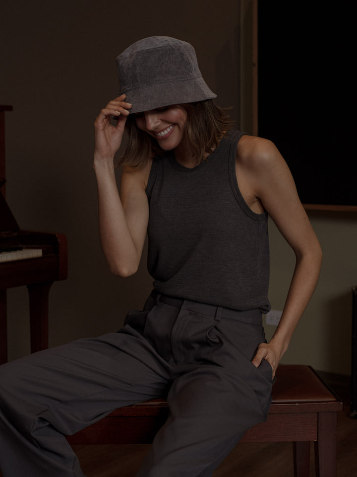 Modelo usando una camiseta color gris con cuello halter y manga sisa con un pantalón