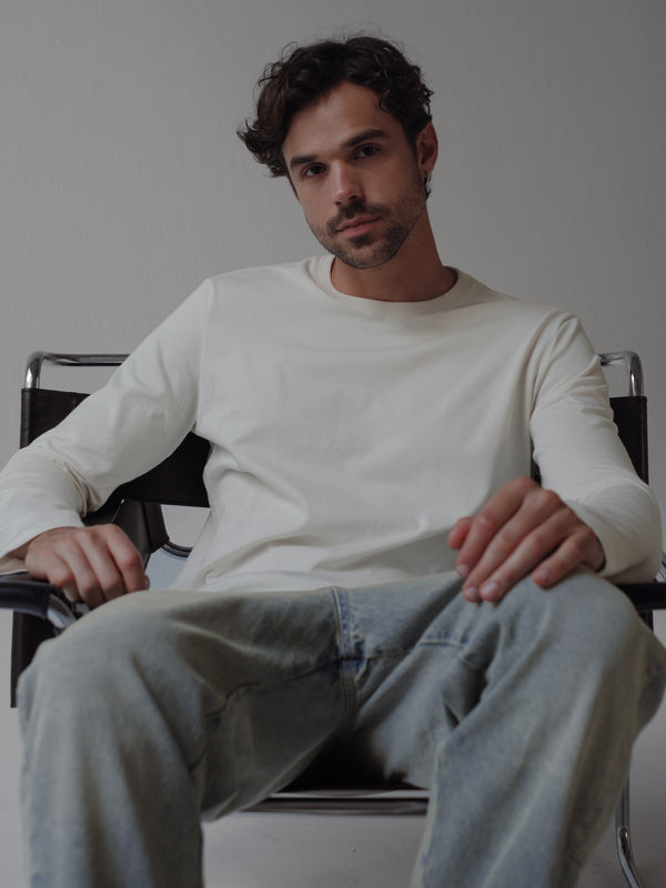 Modelo sentado usando camiseta manga larga fit regular color crudo.