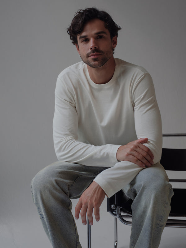 Modelo sentado usando jean y camiseta crudo manga larga fit regular. 