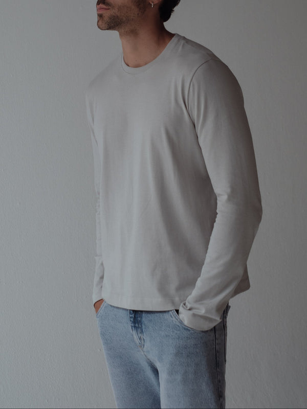 Modelo usando camiseta gris manga larga con jean azul claro. 