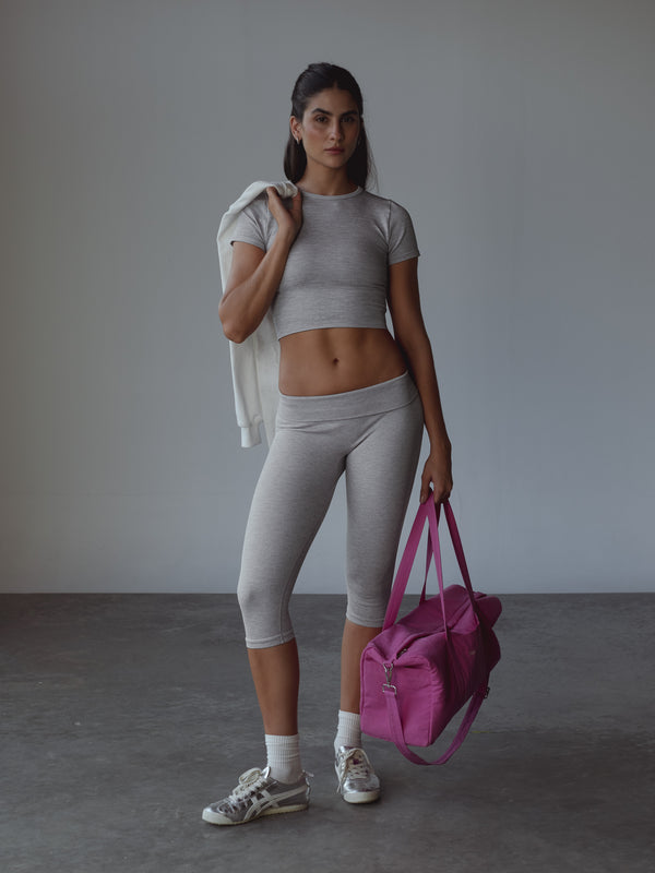 Modelo usando set deportivo gris, medias midi blancas y llevando un bolso fucsia en la mano.