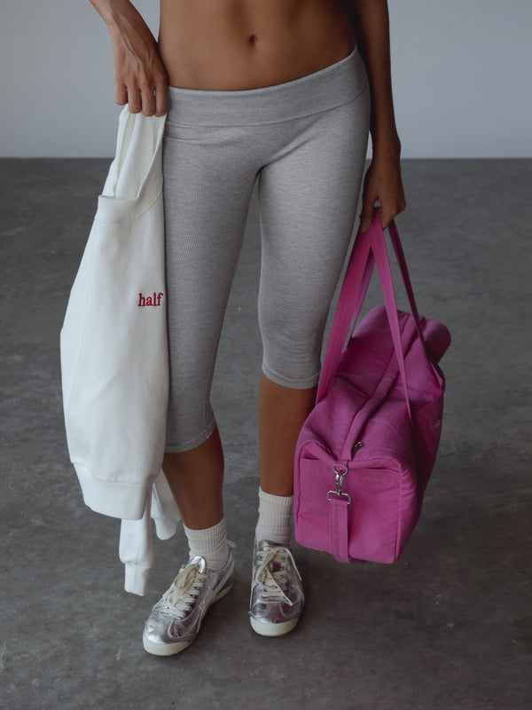 Modelo usando capri gris y medias midi blancas, con un buzo blanco y un bolso fucsia en la mano.