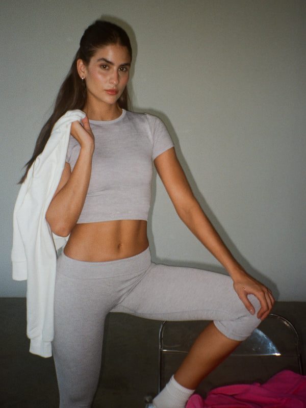 Modelo usando set deportivo gris y lleva un buzo blanco en el hombro.