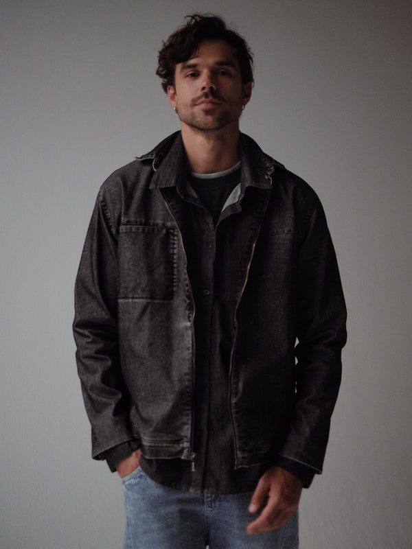 Vista frontal de chaqueta negra con cremallera, bolsillos laterales y cuello.