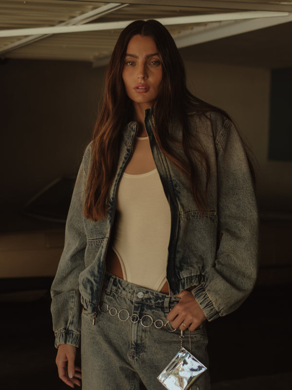 Modelo usando bodie y jean con chaqueta bomber denim con cremallera.