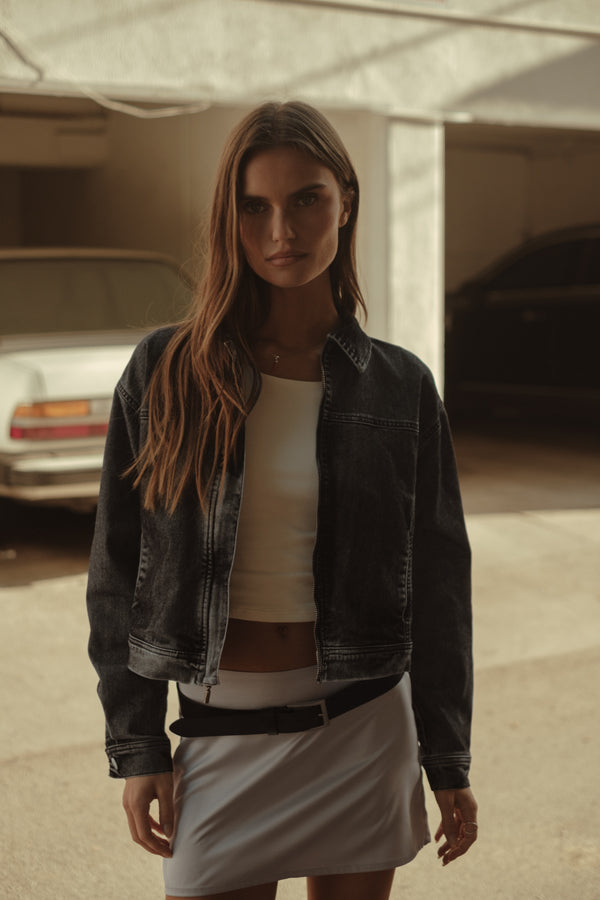 Modelo usando chaqueta negra con top crudo y falda plata con cinturón.