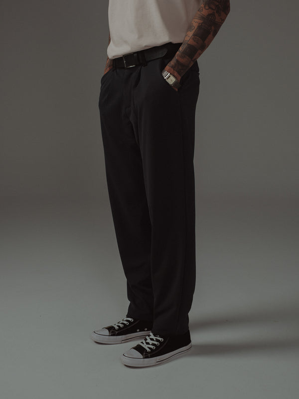 Vista lateral modelo con pantalón negro, cinturón de cuero y tenis.