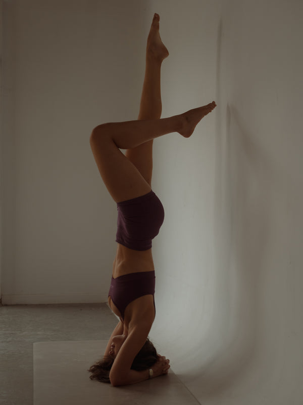 Modelo practicando yoga con ropa deportiva en poliamida color vino.