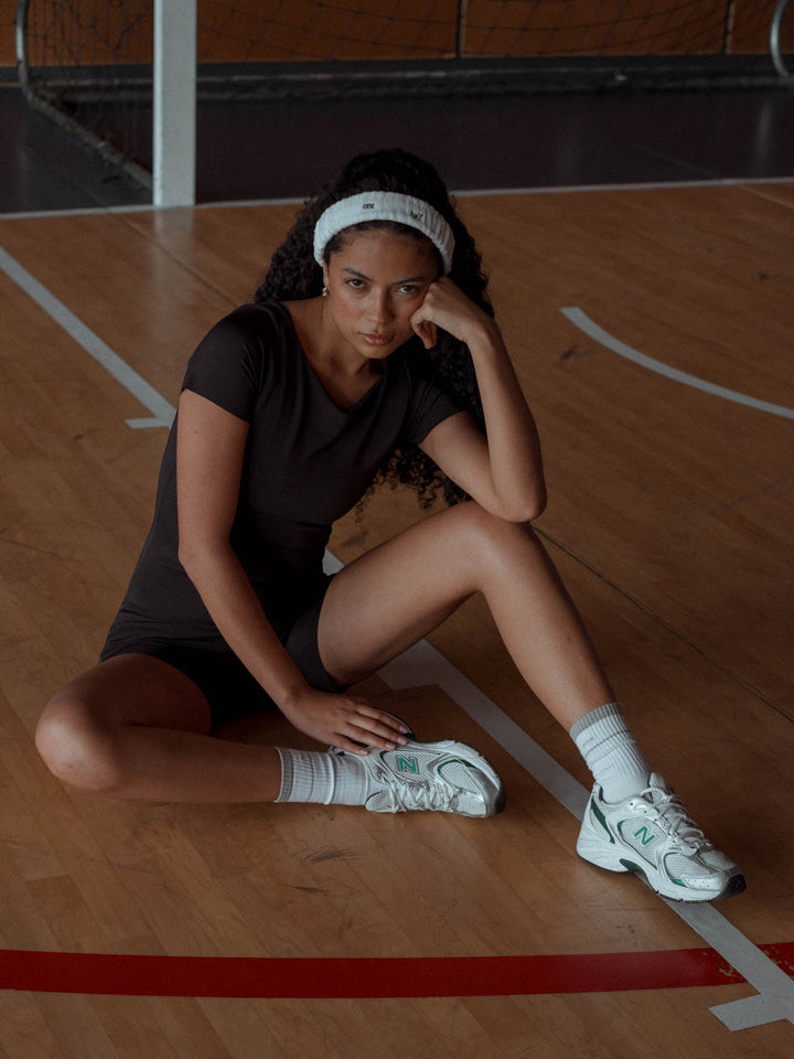La modelo está sentada sobre cancha de basquet usando enterizo deportivo color negro,