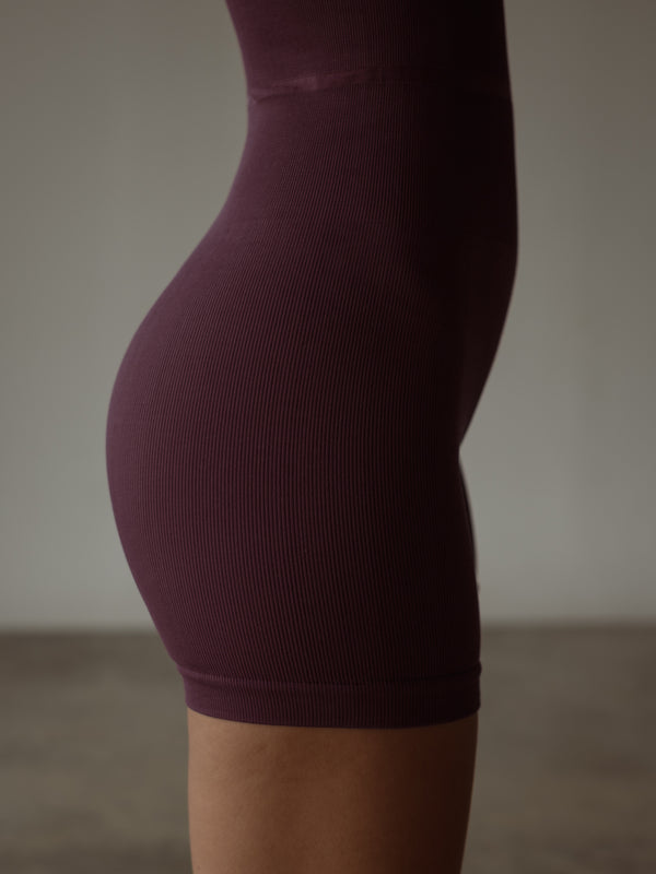 Vista lateral enterizo deportivo vino de short con control abdomen.