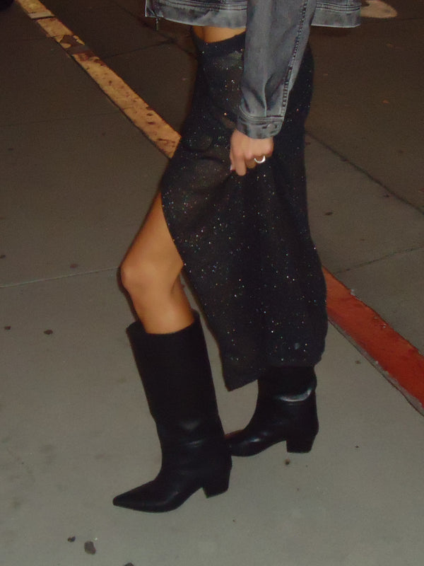 Vista lateral de falda negra con transparencia, brillo y abertura.