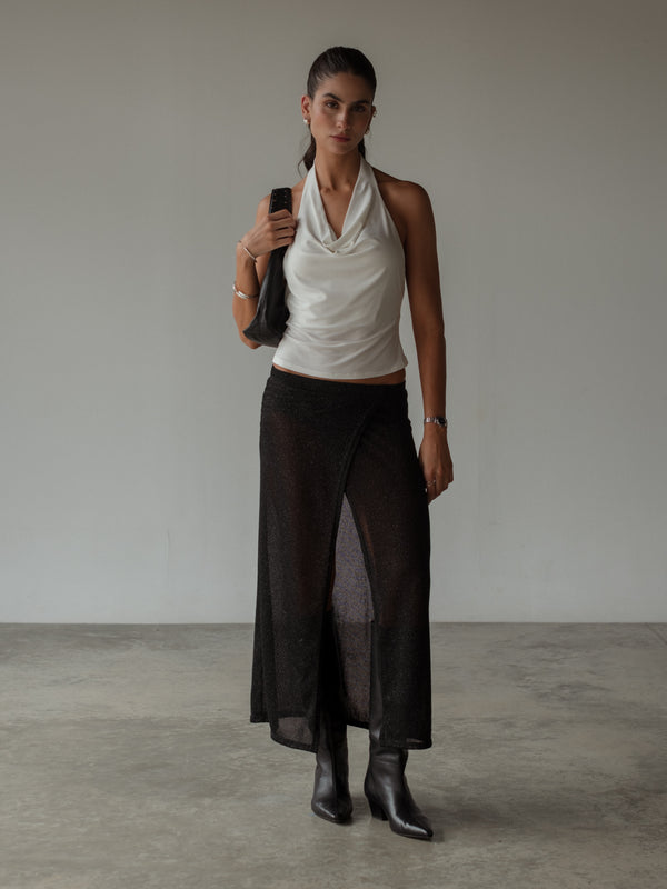 Modelo usando top escote drapeado y falda negra con brillos y botas.