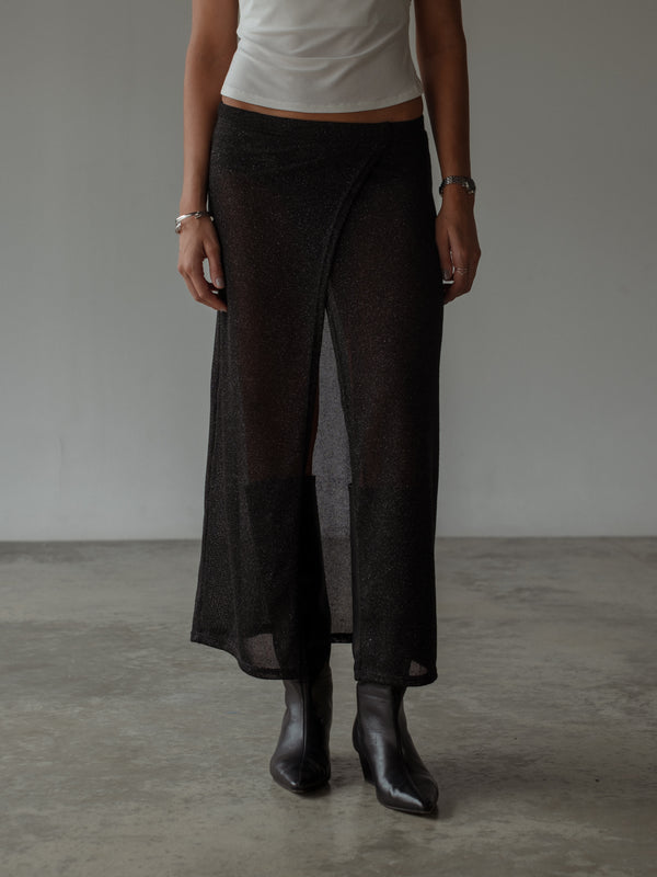 Vista frontal de falda negra con botas, top crudo y accesorios plata.