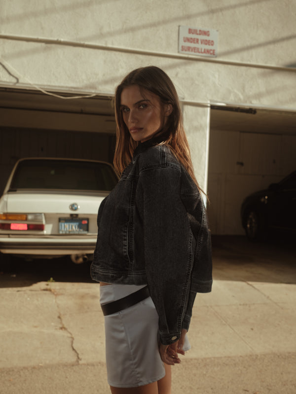 Vista lateral de modelo con mini falda de satín plata con chaqueta negra.