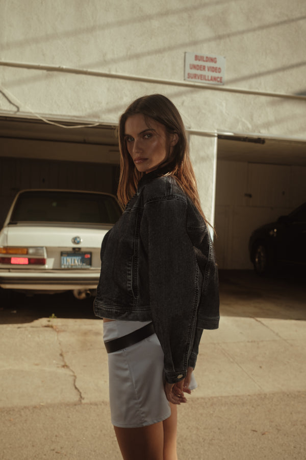 Vista lateral de modelo con mini falda de satín plata con chaqueta negra.