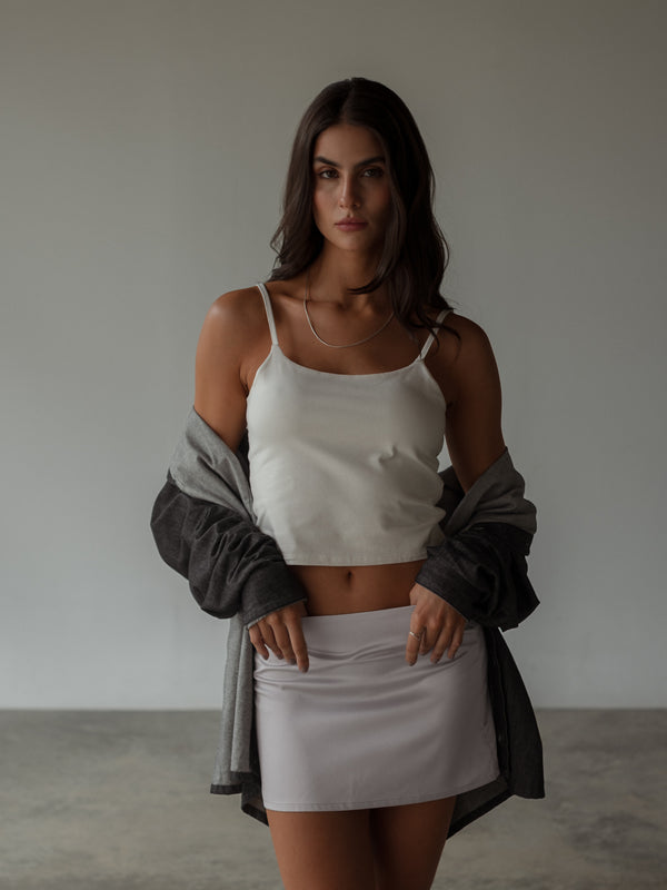 Modelo usando camisa negra con crop top y mini falda plata satinada.