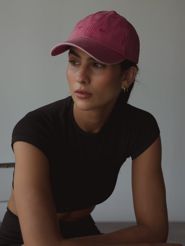 Modelo mirando a un lado usando gorra fucsia con efecto desgaste.