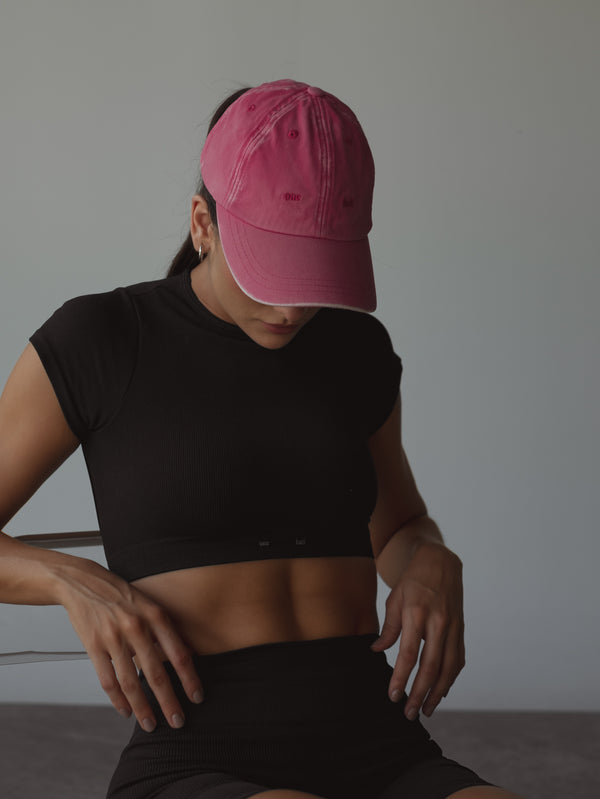 Modelo con set deportivo negro y gorra fucsia.