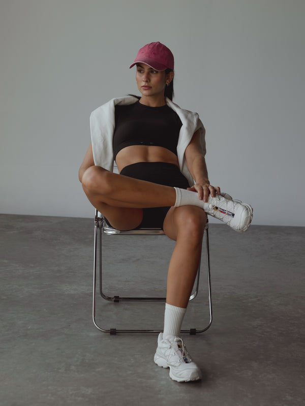 Modelo sentada vistiendo gorra fucsia vibrante y set deportivo negro.