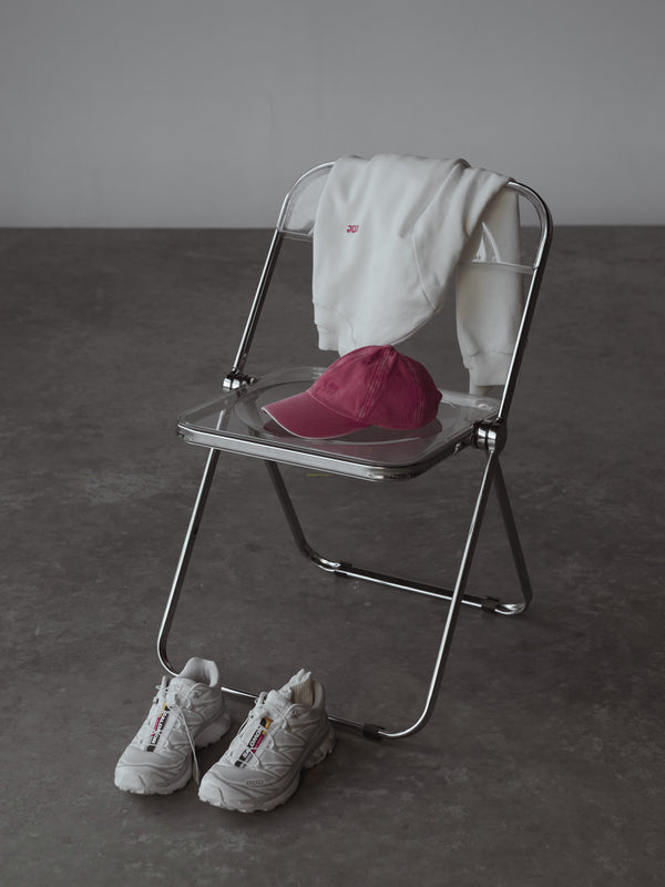 Silla con buzo blanco, gorra fucsia y en el piso zapatos blancos.