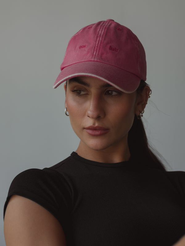 Modelo usando gorra fucsia con efecto desgastado y bordado “One Half” adelante.