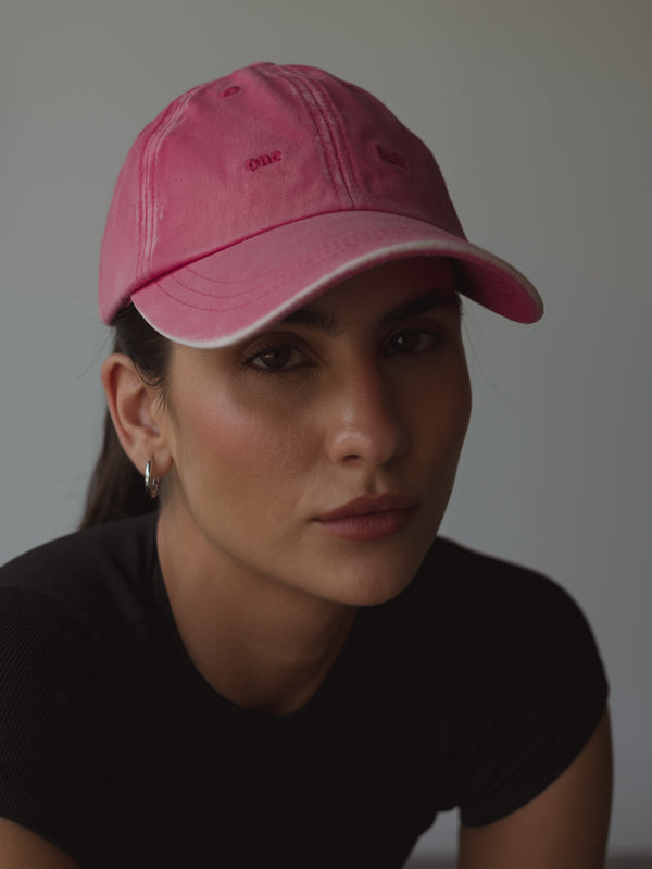 Modelo con cabello recogido usando gorra fucsia.