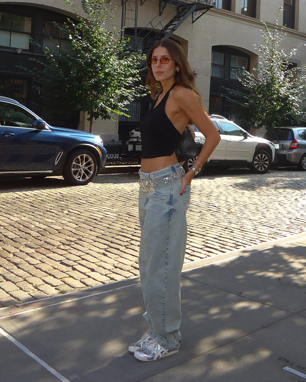 Vista posterior top negro cruzado en la espalda con jean ancho y tenis. 