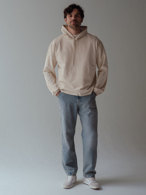 Modelo usando buzo con capucha y cordón color crema y jean azul.