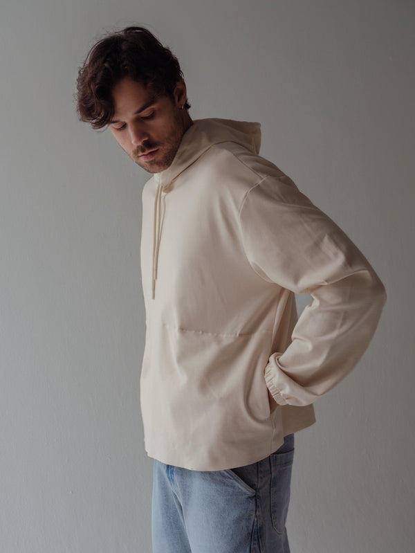 Modelo con las manos en los bolillos laterales de buzo color crema. 