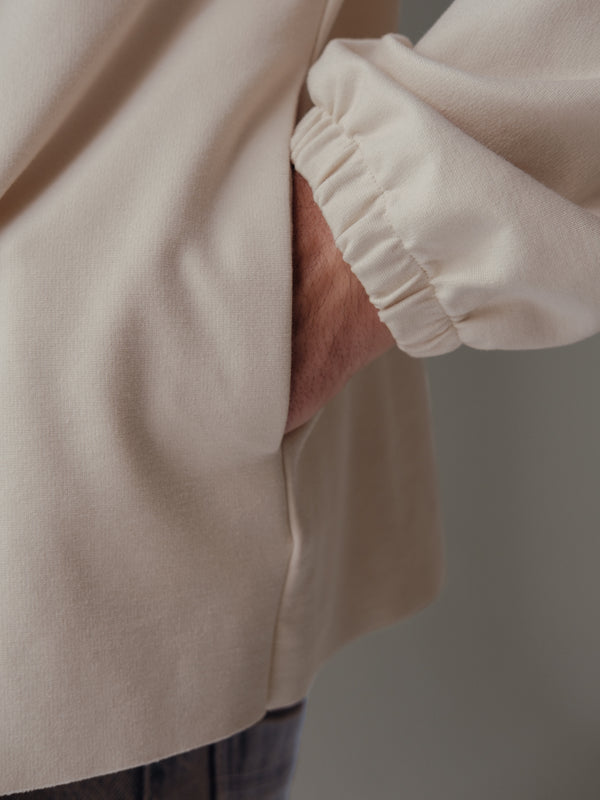 Vista a detalle de bolsillos laterales de buzo crema con elástico en manga.