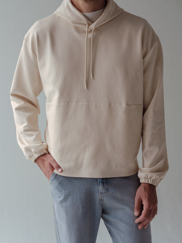 Vista frontal de buzo crema con capucha, cordón y elástico en mangas.