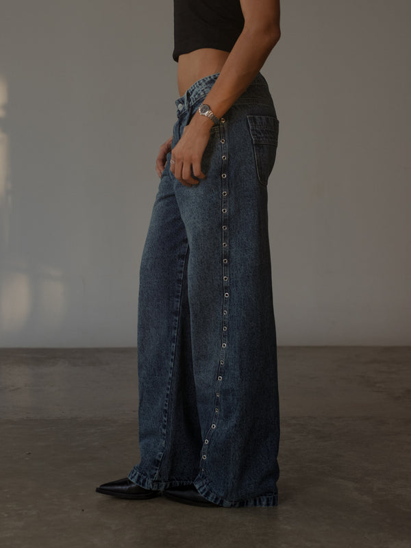 Vista lateral de modelo usando jean azul con apliques metálicos plata.