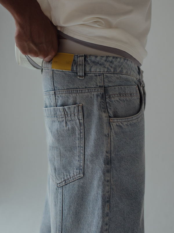 Vista posterior a detalle bolsillos y garra amarilla de jean azul claro para hombre. 