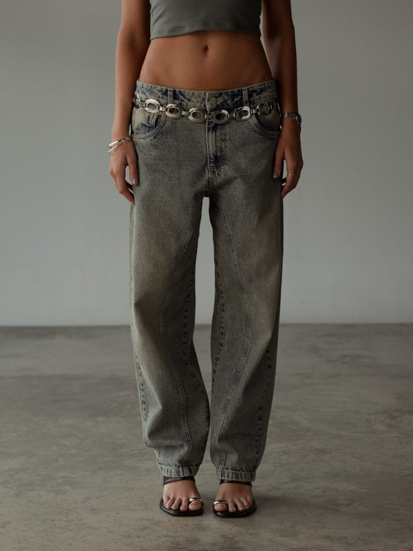 Vista frontal jean bota ancha lavado vintage con cinturón metálico.