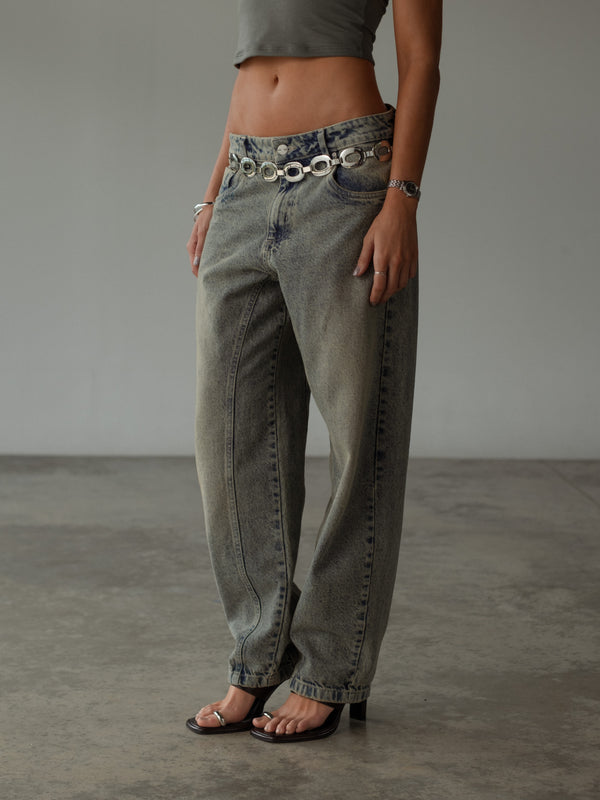 Modelo con jean bota ancha lavado vintage con sandalias y top gris.