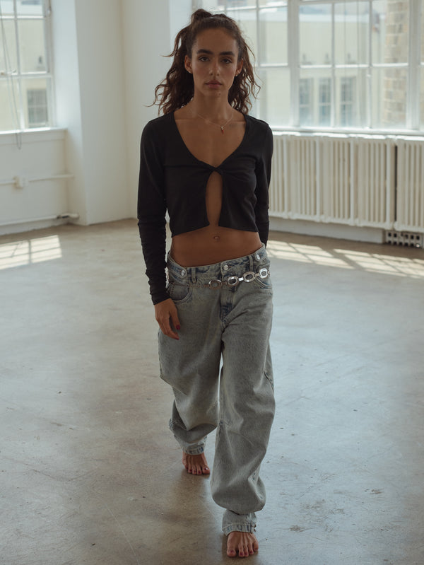 Modelo usando jean azul claro ancho con top escotado negro manga larga. 