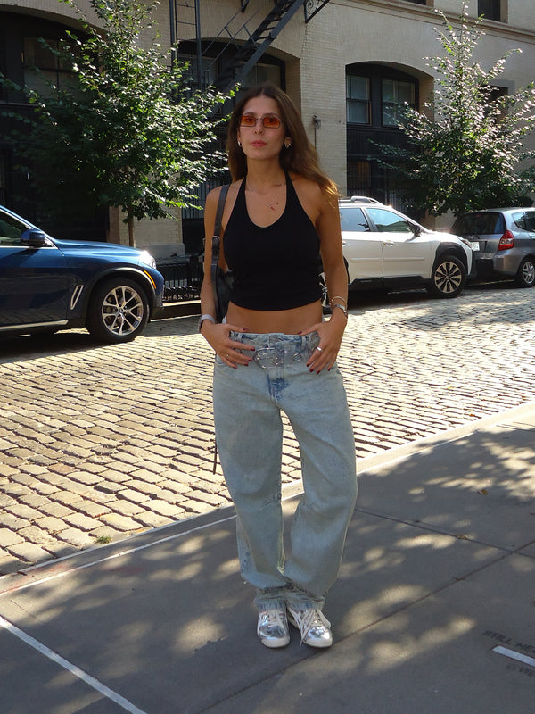 Modelo en la calle en día soleado con jean azul ancho y top negro escote U.