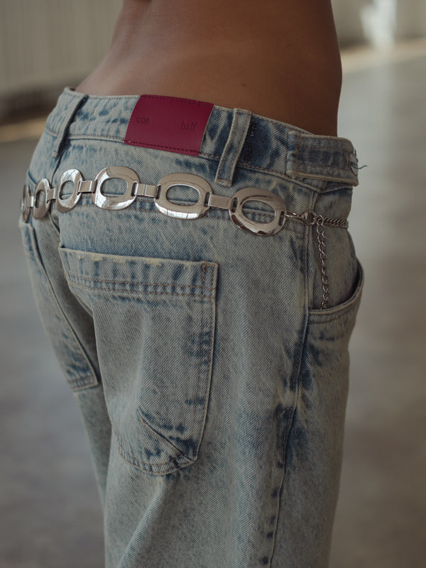 Vista posterior a detalle de pretina de jean azul con garra en fucsia. 