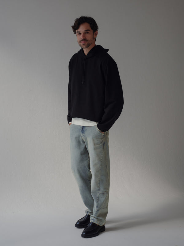 Modelo con manos en los bolsillos usando buzo negro y jean azul. 