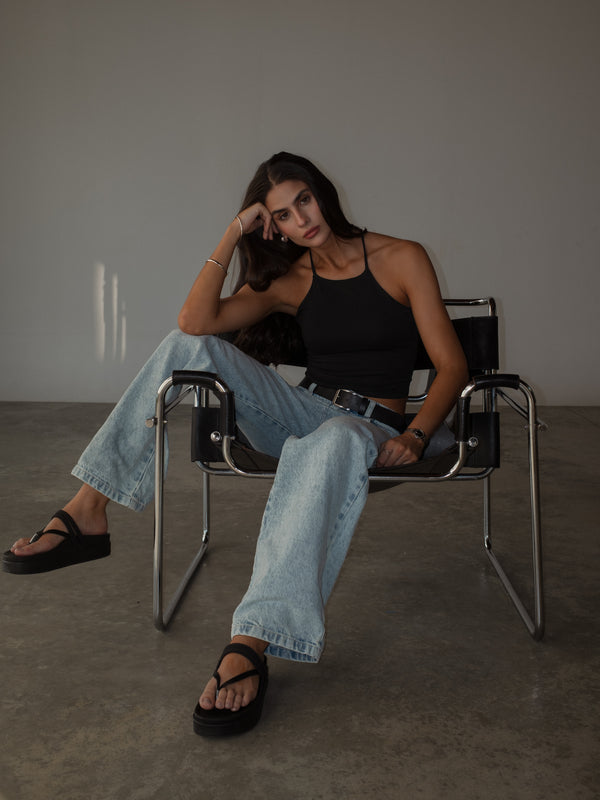 Modelo sentada usando jean bota recta azul claro con top y sandalias.