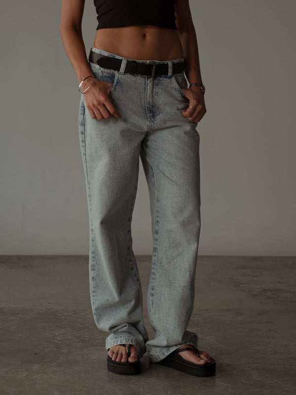 Vista frontal de jean azul claro con cinturón negro y crop top negro.