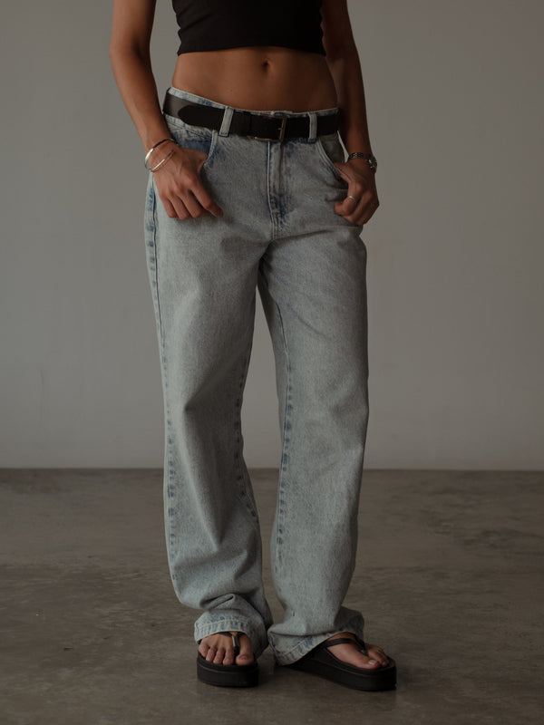 Vista frontal de jean azul claro con cinturón negro y crop top negro.