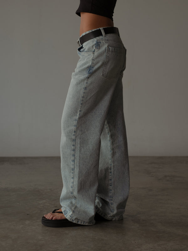 Vista lateral de modelo usando jean clásico azul claro con crop top negro.