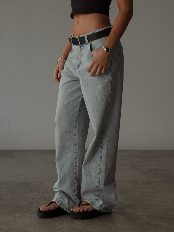 Modelo usando jean clásico azul bota recta con cinturón, sandalias y top.