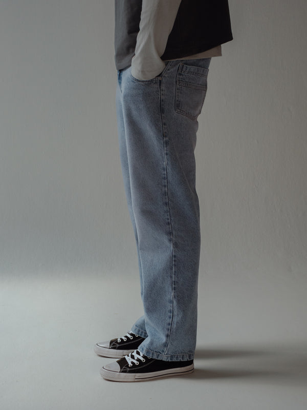 Vista lateral jean de hombre azul claro bota recta con tenis negros. 