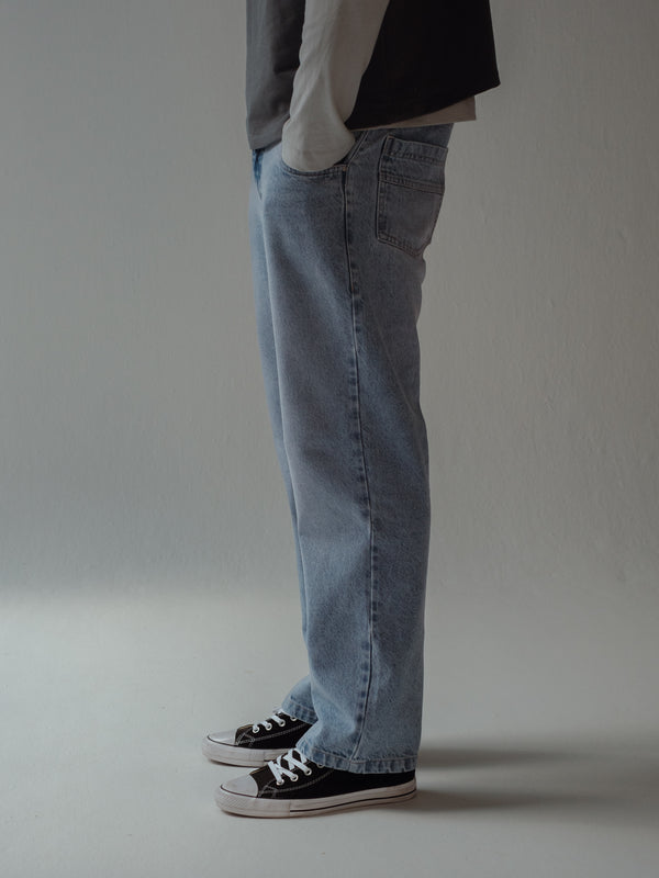 Vista lateral jean de hombre azul claro bota recta con tenis negros. 