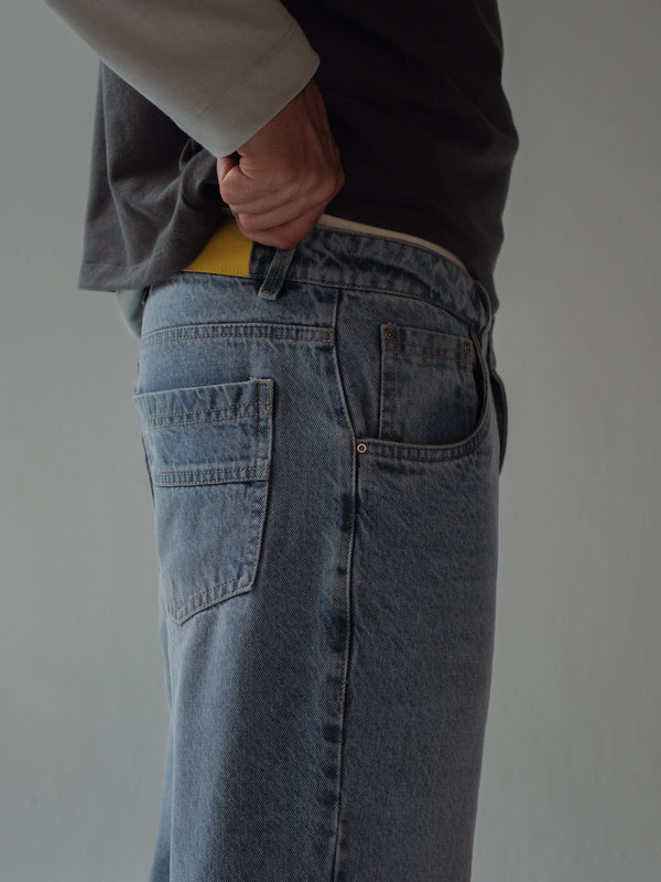 Vista lateral a detalle bolsillo con relojera y garra amarilla de jean azul claro. 