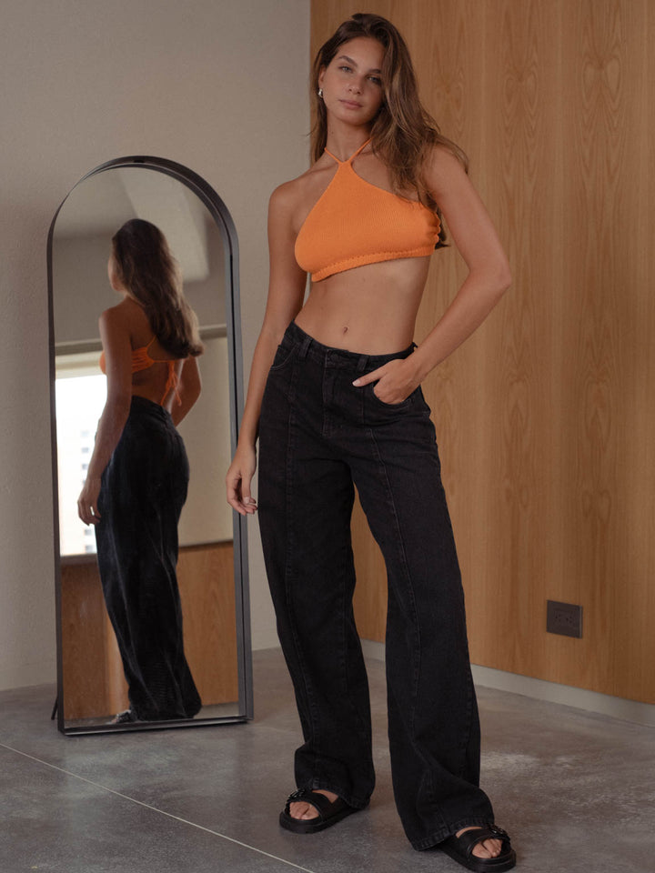 Vista completa de la modelo usando jean negro y top naranja. 