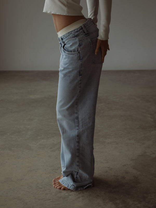 Vista lateral modelo con jean azul clásico y top crudo manga larga.