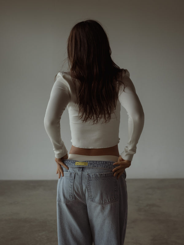 Vista posterior modelo con jean azul de bolsillos con top crudo manga larga.